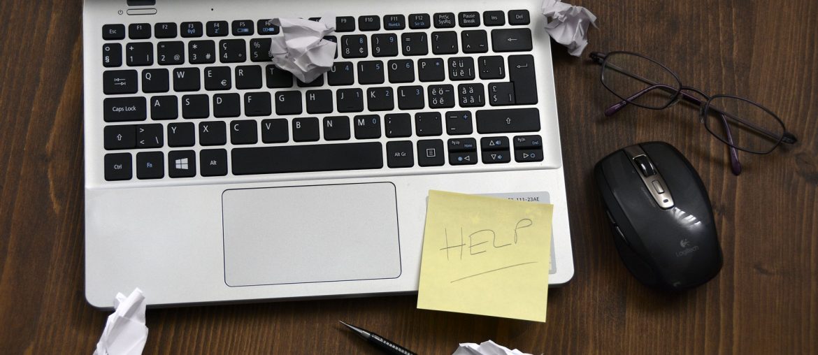 How to Test Your Website on Another Server Before It is Pointed There (a.k.a. How to modify and use your “hosts” file) Laptop with crumpled paper, a sticky note with Help, glasses, a pen, and a mouse on a wooden desk.