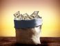 A sack overflowing with US dollar bills on a wooden table against a warm, textured yellow background.