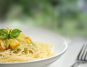 Plate of spaghetti with creamy pesto sauce topped with grilled vegetables and fresh basil, fork beside the dish.