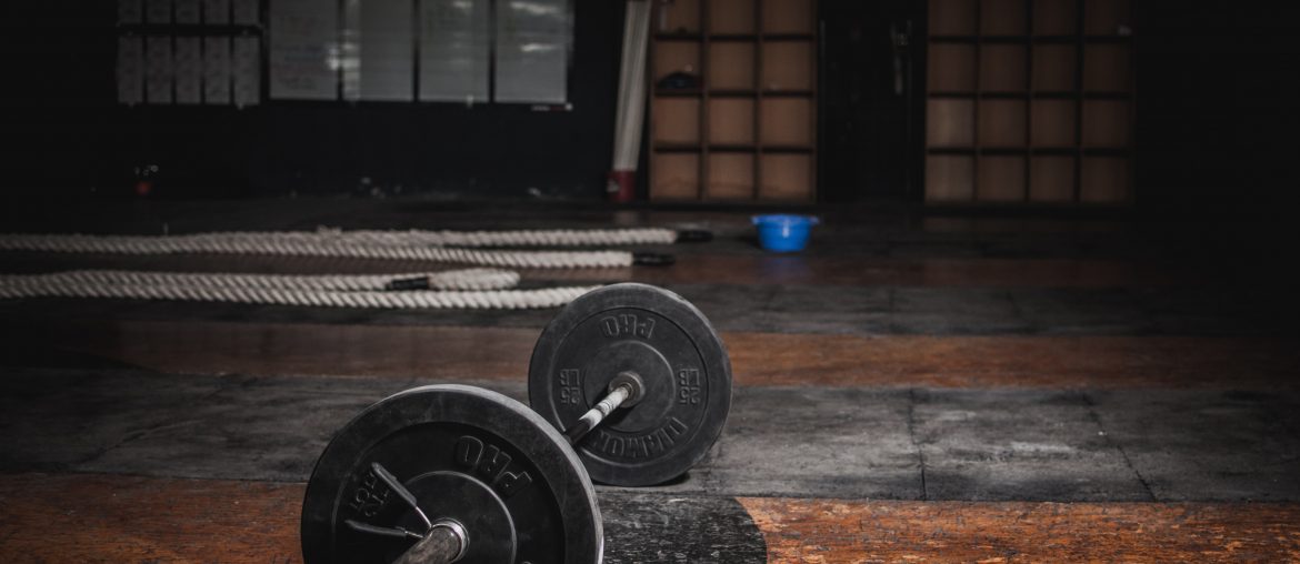 Barbell resting on gym floor with ropes and equipment in background, suggesting a strength training environment.