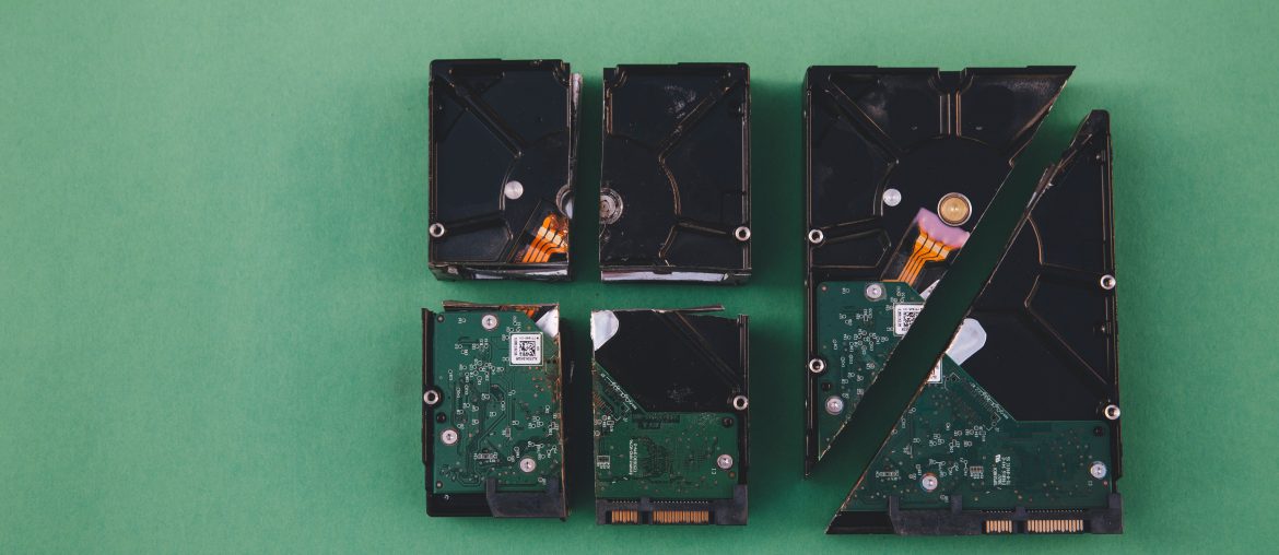 Four broken hard drives on a green background arranged in pieces symbolizing data loss or destruction.