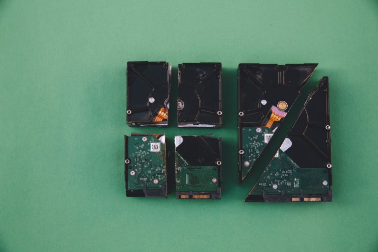 Four broken hard drives on a green background arranged in pieces symbolizing data loss or destruction.