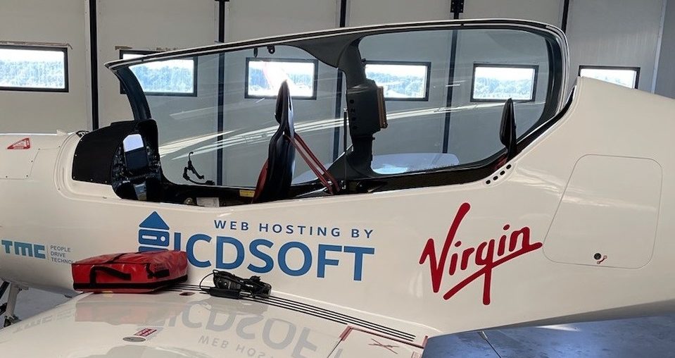 Cockpit of a small white aircraft with Virgin and ICDSoft branding inside a hangar, featuring large side windows.