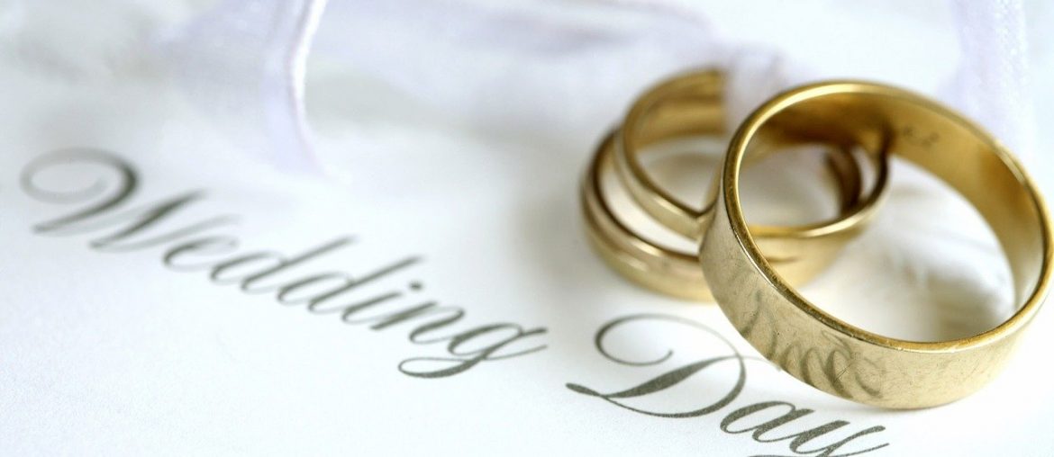 Building a Wedding Website? Here is What You Need on It Gold wedding rings on a white invitation card with elegant script reading Wedding Day and a ribbon accent.