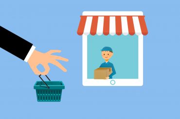 Hand holding shopping basket with delivery worker on tablet screen, symbolizing online shopping and delivery service.