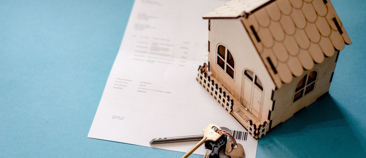 8 Features You Need on a Real Estate Website Small house model on top of home loan document with keys on blue background, symbolizing real estate purchase.