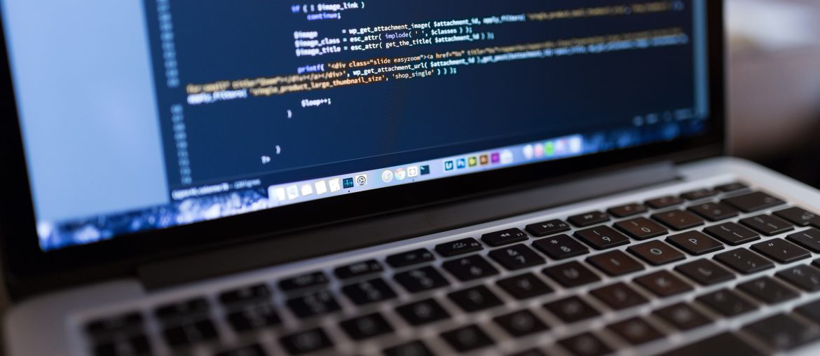 Template vs Custom-made Website – Which One is Better? Laptop displaying complex code on a screen, reflecting a programming or web development environment.