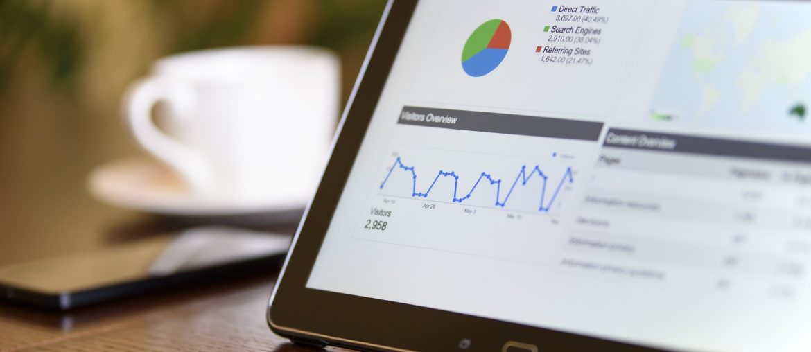 Tablet displaying digital analytics dashboard with traffic overview, pie chart, and graphs on wooden desk.