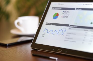 Tablet displaying digital analytics dashboard with traffic overview, pie chart, and graphs on wooden desk.