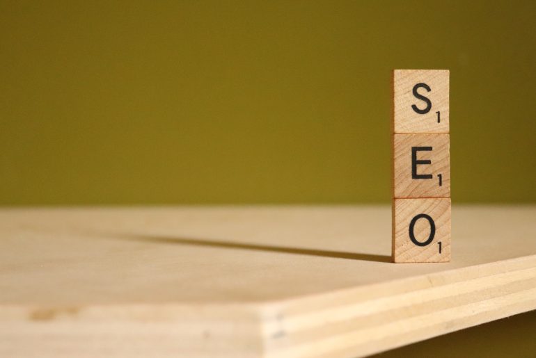 Wooden blocks spelling SEO stacked vertically on a wooden surface with a green background