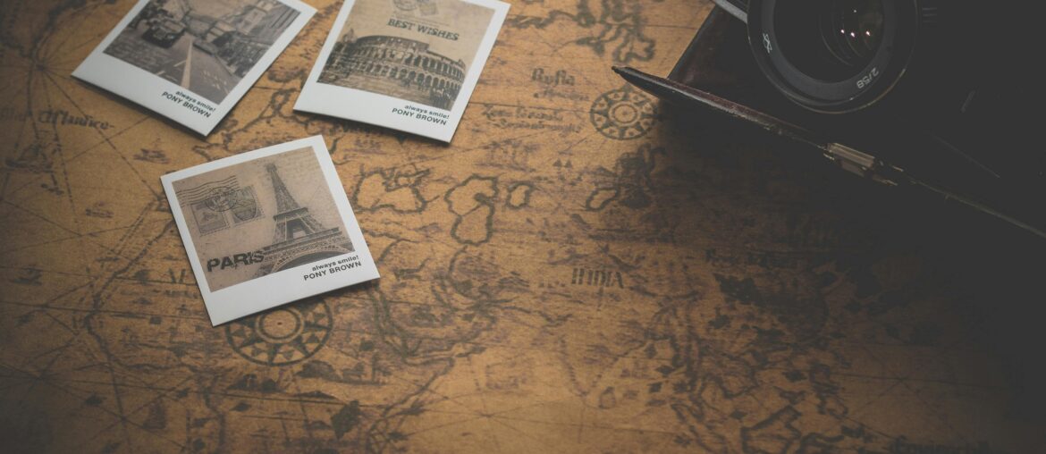Vintage camera on an old world map with three travel-themed postcards, featuring famous landmarks like the Eiffel Tower.